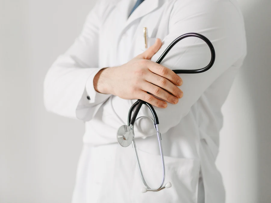 Un medico in camice bianco, a braccia conserte, con uno stetoscopio in mano