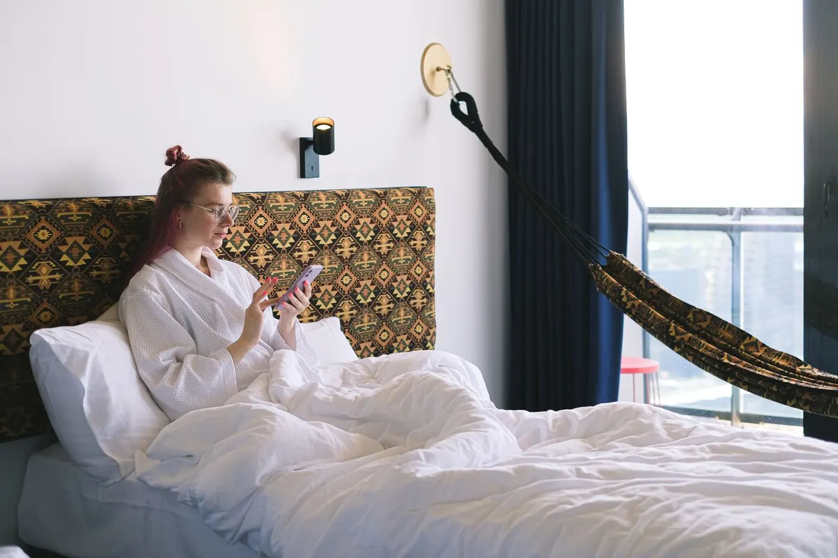 Una viaggiatrice guarda il telefono dal letto di un albergo